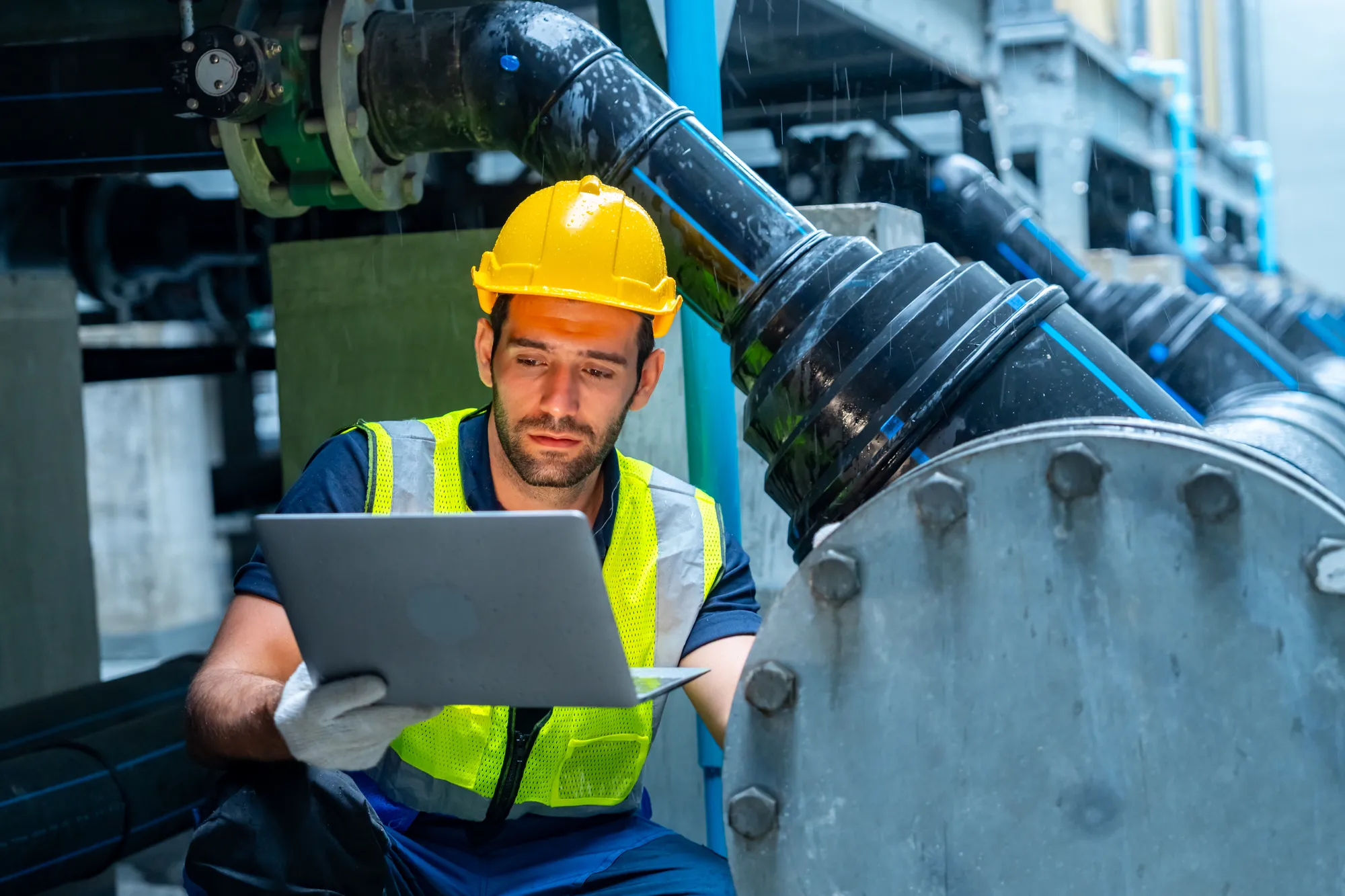 A utility technician with a laptop inspecting industrial pipework at a plant